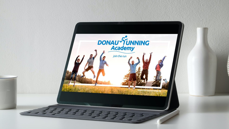 Tablet auf Schreibtisch zeigt DONAURUNNING Academy Banner mit springenden Läufern