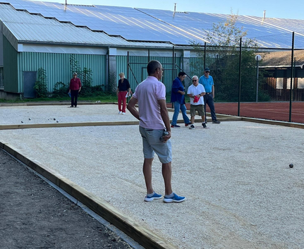Mann im Vordergrund hält Kugel auf Bouleplatz weitere Spieler im Hintergrund