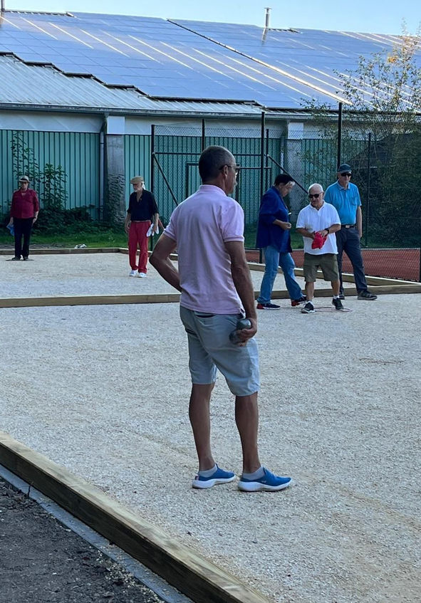 Mann im Vordergrund hält Kugel auf Bouleplatz weitere Spieler im Hintergrund