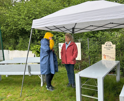 Zwei Personen unter Pavillon im Regen Schild TK ULM Tennisklub Ulm