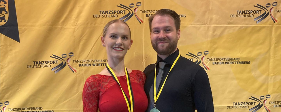 Paar in Tanzkleidung mit Medaillen vor Tanzsport Deutschland Banner