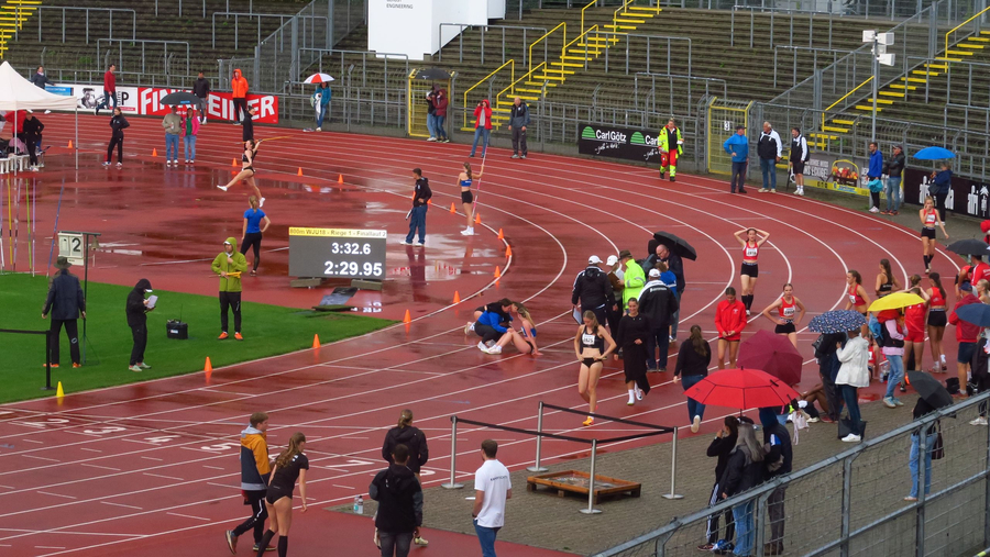 Regennasse Laufbahn mit Athletinnen Zuschauern und Anzeigetafel 3:32.6 2:29.95