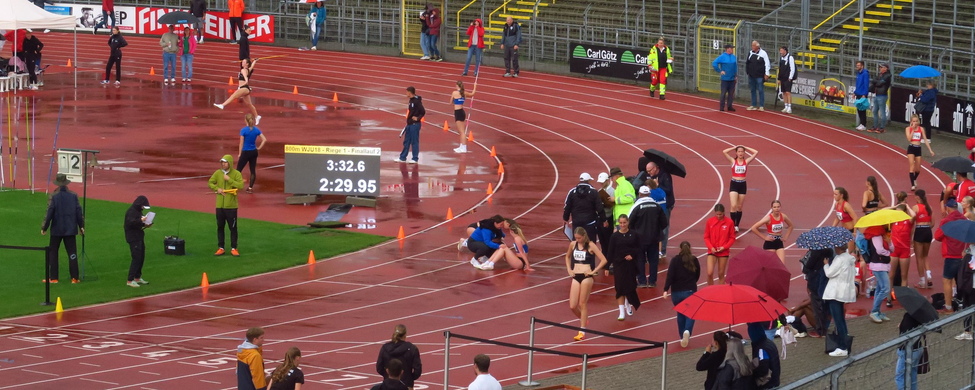 Regennasse Laufbahn mit Athletinnen Zuschauern und Anzeigetafel 3:32.6 2:29.95