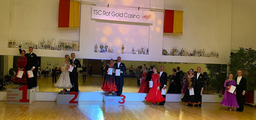 Tanzpaare auf Podest vor Spiegelwand, Banner TSC Rot Gold Casino