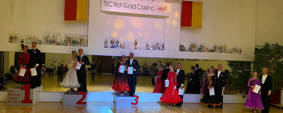 Tanzpaare auf Podest vor Spiegelwand, Banner TSC Rot Gold Casino