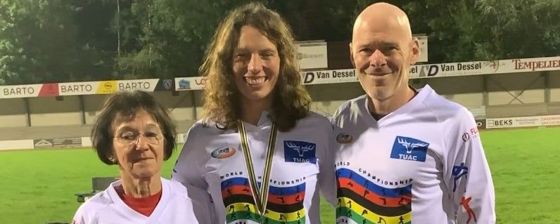 Drei Personen in Wettkampftrikots mittlere Person trägt Medaille