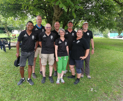 Acht Personen in schwarzen Vereins-Shirts stehen auf einer Wiese unter einem Baum