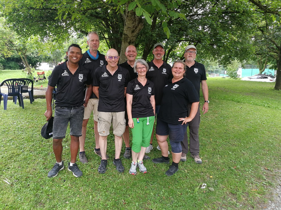 Acht Personen in schwarzen Vereins-Shirts stehen auf einer Wiese unter einem Baum