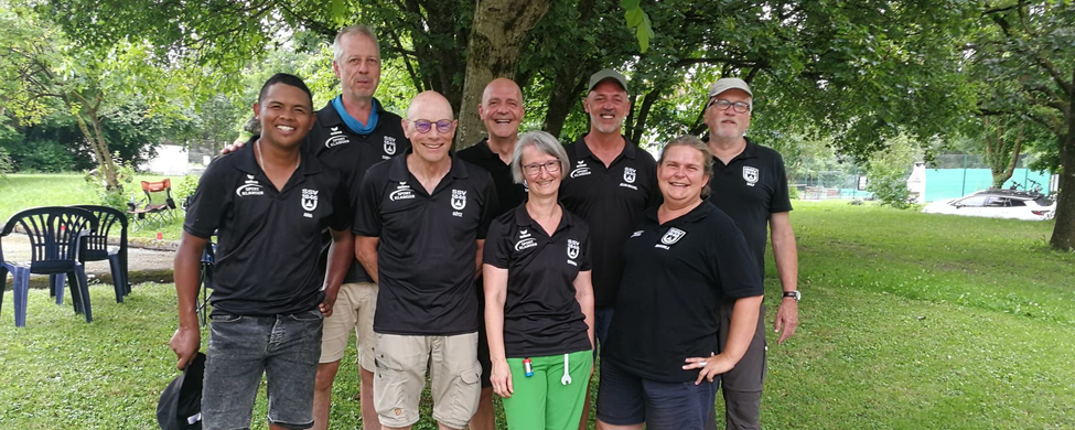 Acht Personen in schwarzen Vereins-Shirts stehen auf einer Wiese unter einem Baum