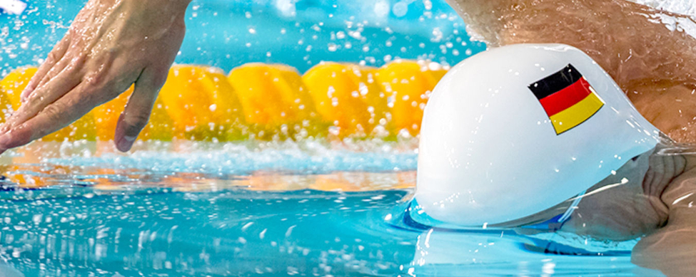 Schwimmer mit weißer Badekappe und deutschem Flaggenaufkleber schwimmend im Wettkampfbecken