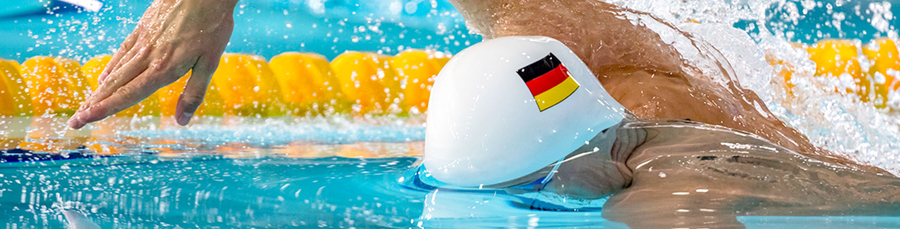 Schwimmer mit weißer Badekappe und deutschem Flaggenaufkleber schwimmend im Wettkampfbecken