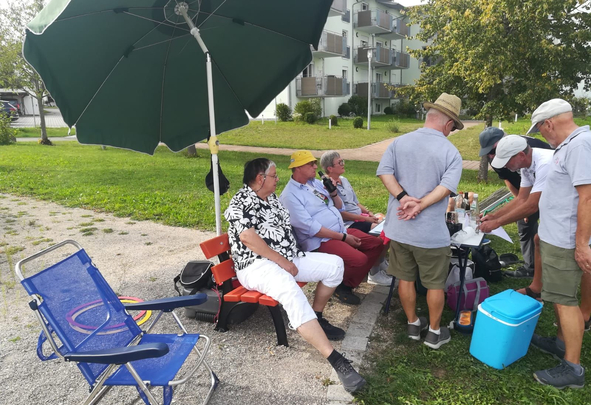 Gruppe älterer Personen unter Sonnenschirm an Klapptisch mit Getränken