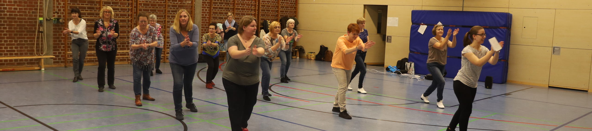Mehrere Frauen in Turnhalle tanzen und klatschen in Reihen