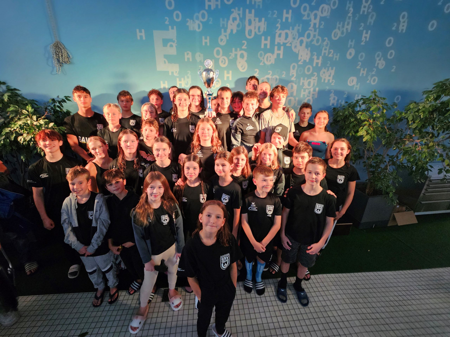 Junge Schwimmerinnen und Schwimmer in Teamtrikots mit Pokal