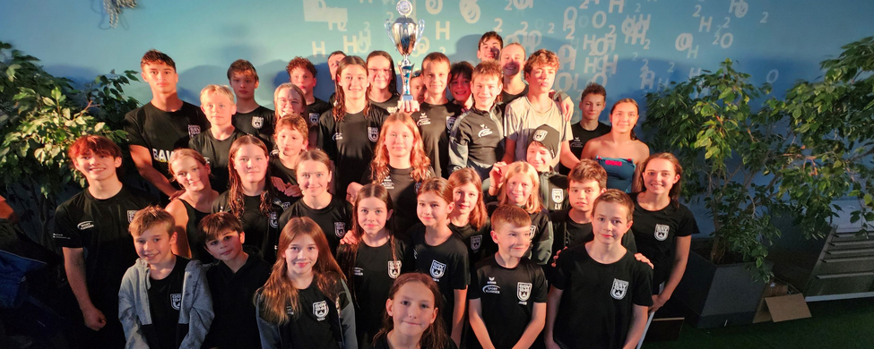 Junge Schwimmerinnen und Schwimmer in Teamtrikots mit Pokal