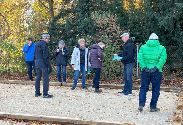 Gruppe von sieben Personen spielt Boule auf Kiesbahn im Herbst