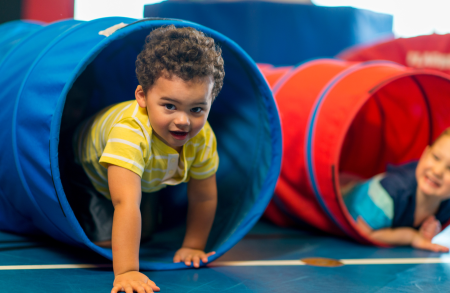 Kleinkind krabbelt durch blauen Spieltunnel in Turnhalle