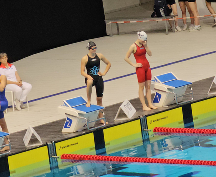 Drei Schwimmerinnen auf Startblöcken vor Wettkampfbecken