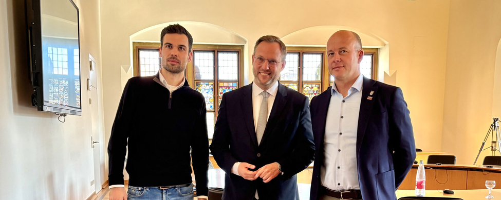 Drei Männer posieren im Ratssaal nach Pressekonferenz