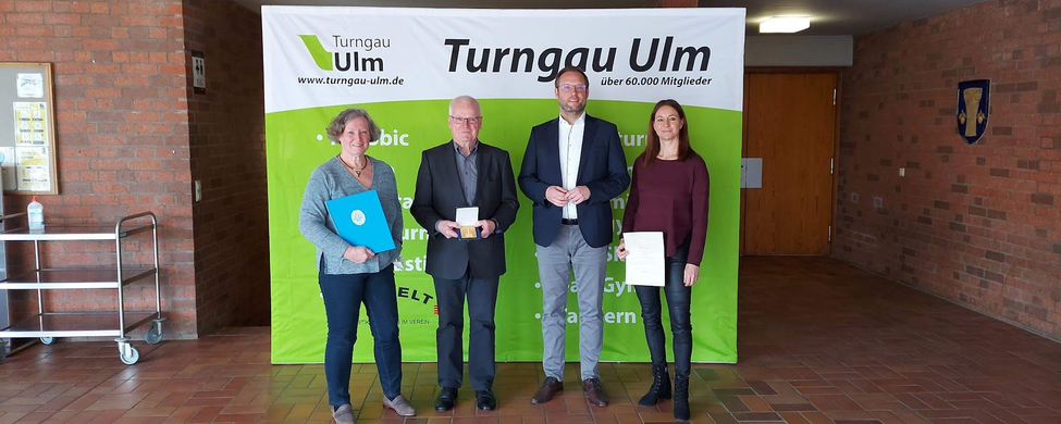 Vier Personen vor Turngau Ulm Banner zwei mit Urkunden eine mit Medaille