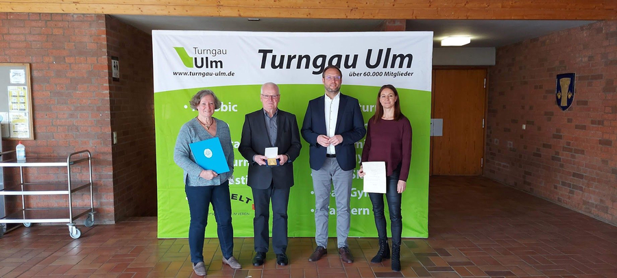 Vier Personen vor Turngau Ulm Banner zwei mit Urkunden eine mit Medaille