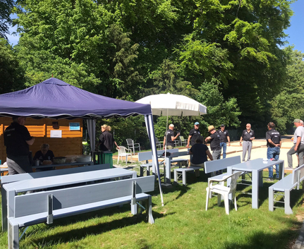 Gruppe von Menschen bei Veranstaltung mit Tischen Bänken Zelt und Sonnenschirm