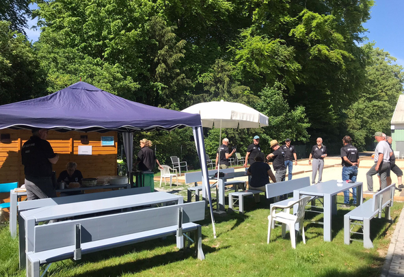 Gruppe von Menschen bei Veranstaltung mit Tischen Bänken Zelt und Sonnenschirm