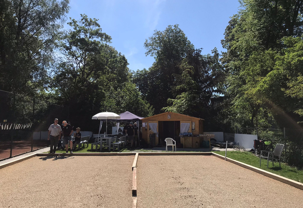 Boule-Bahn vor Holzhütte mit Sonnenschirmen und Personen