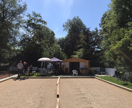Boule-Bahn vor Holzhütte mit Sonnenschirmen und Personen