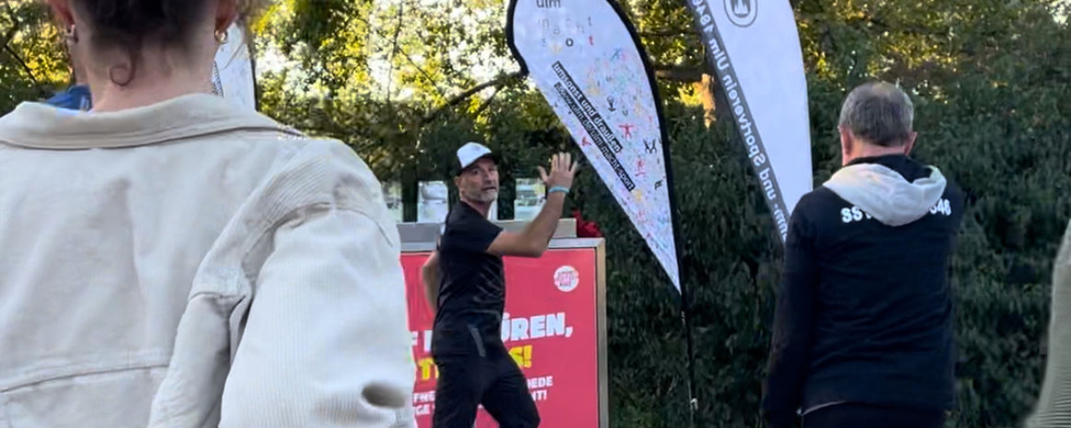 Trainer macht Aufwärmübung vor roter SportBOX, Teilnehmende folgen