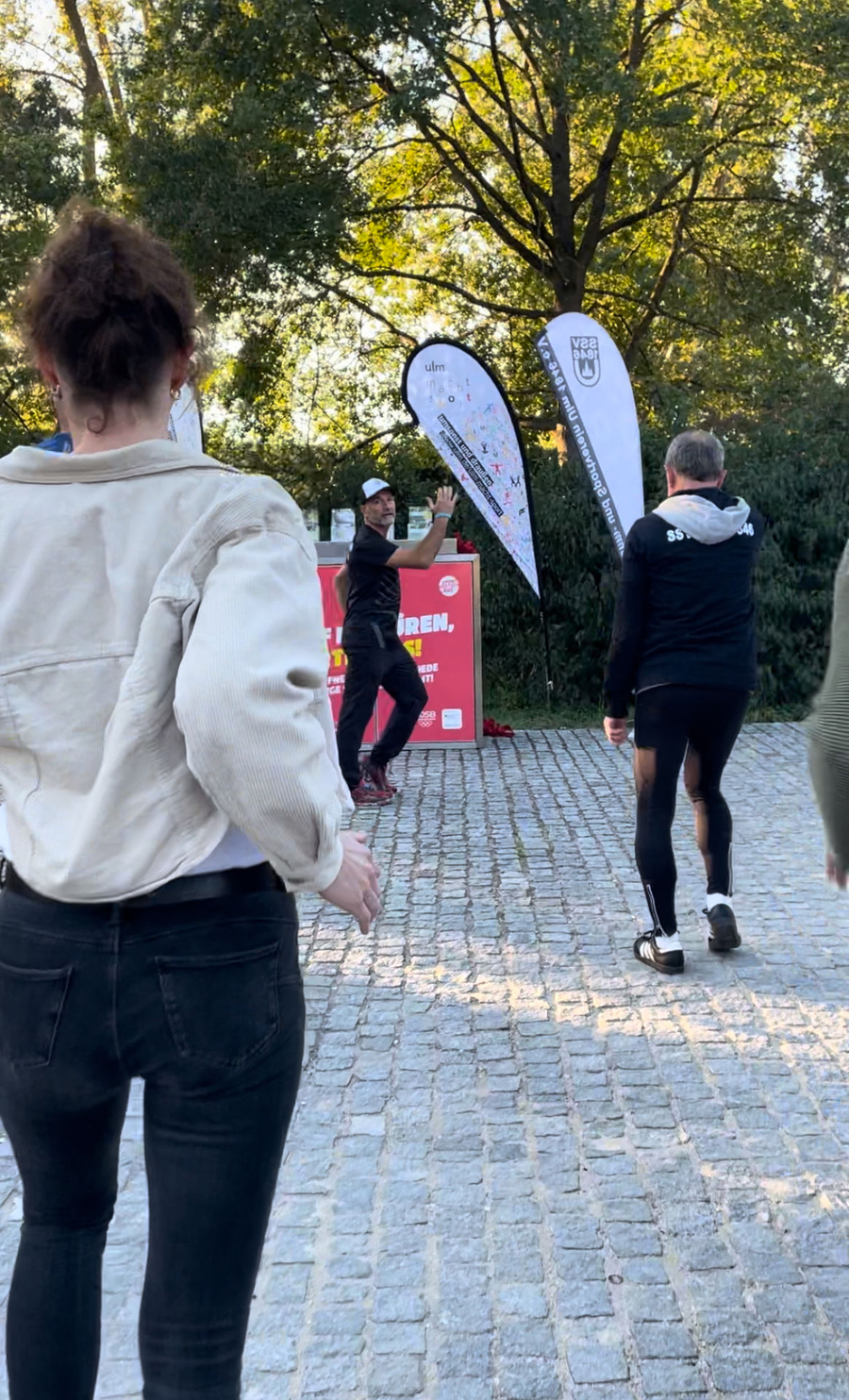 Trainer macht Aufwärmübung vor roter SportBOX, Teilnehmende folgen