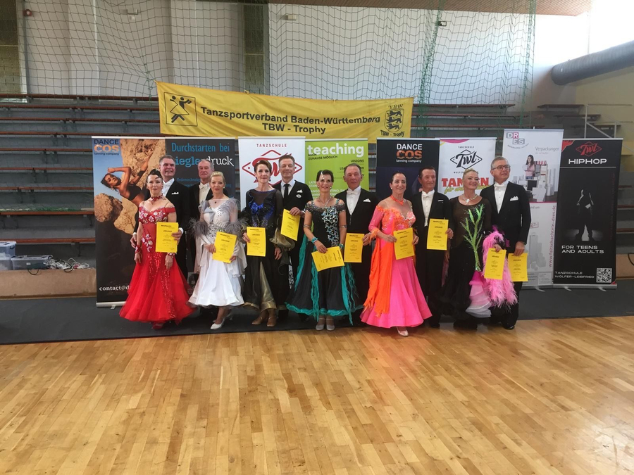 Tanzpaare in Abendkleidung mit Urkunden vor TBW-Trophy Banner