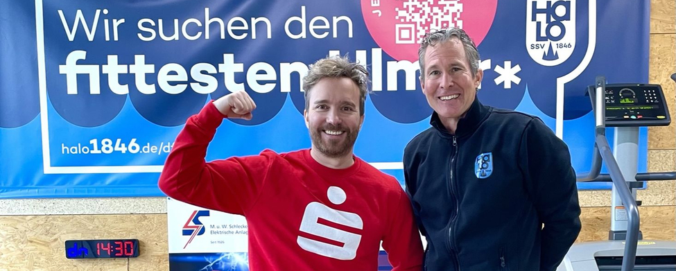 Zwei Männer vor Banner mit Schrift Wir suchen den fittesten Ulmer*