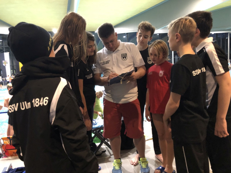 Cheftrainer mit Clipboard umringt von SSV Ulm 1846 Schwimmern