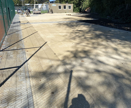 Baustelle mit kompaktierter Kiesfläche Baucontainer Bagger Zaun und Personenschatten
