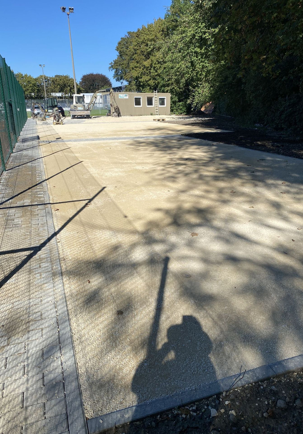 Baustelle mit kompaktierter Kiesfläche Baucontainer Bagger Zaun und Personenschatten