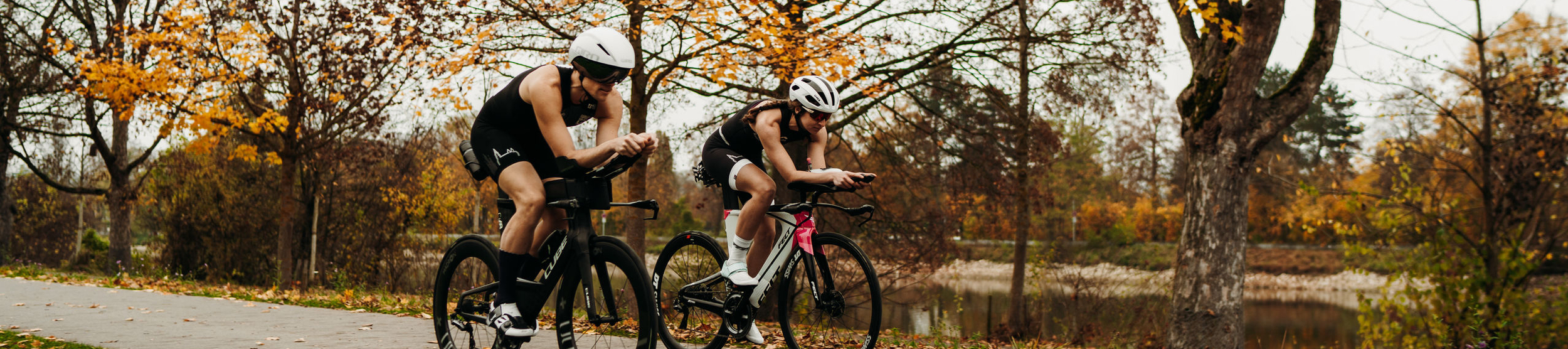 Zwei Radfahrende in Helmen auf Rennrädern im Herbstpark