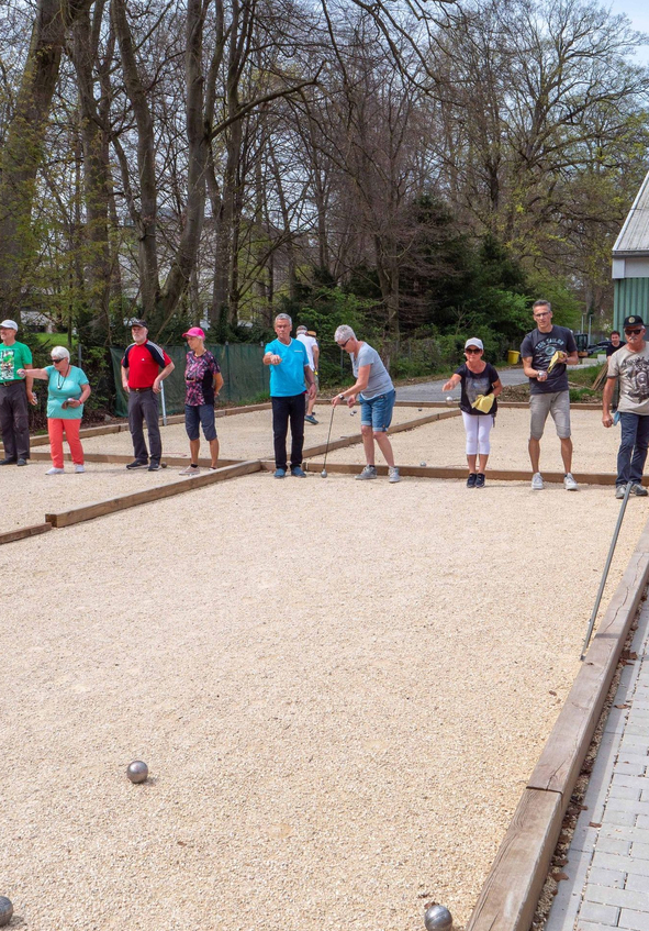 Mehrere Erwachsene spielen Boule auf Kiesbahnen im Freien