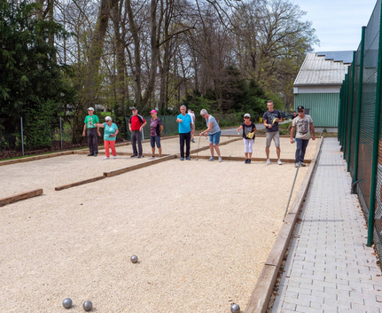 Mehrere Erwachsene spielen Boule auf Kiesbahnen im Freien