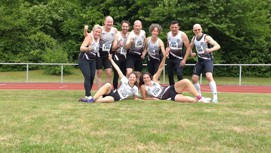 Leichtathletik-Masters Team in schwarz-weißen Trikots jubelnd auf Tartan