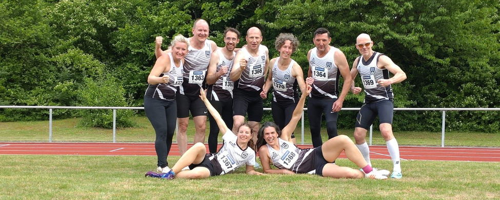 Leichtathletik-Masters Team in schwarz-weißen Trikots jubelnd auf Tartan