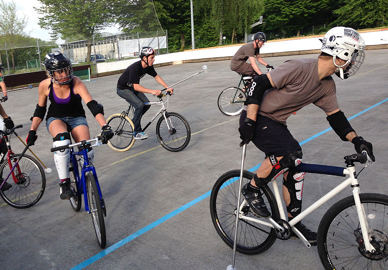 Vier Fahrradpolospieler mit Helmen und Schlägern auf Außenplatz