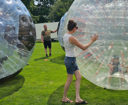 Frau schiebt transparente Zorbkugel mit Kind auf Sportwiese