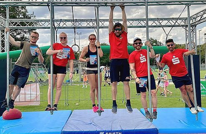 Sechs Erwachsene an Kletterstange über blauen Matten auf Sportplatz