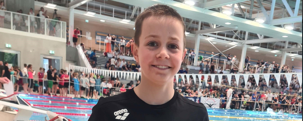 Lächelnder jugendlicher Schwimmer hält Urkunde neben Wettkampfbecken