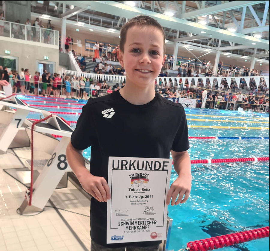 Lächelnder jugendlicher Schwimmer hält Urkunde neben Wettkampfbecken