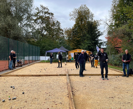 Mehrere Spieler werfen Metallkugeln auf Boule-Bahn mit Zelt