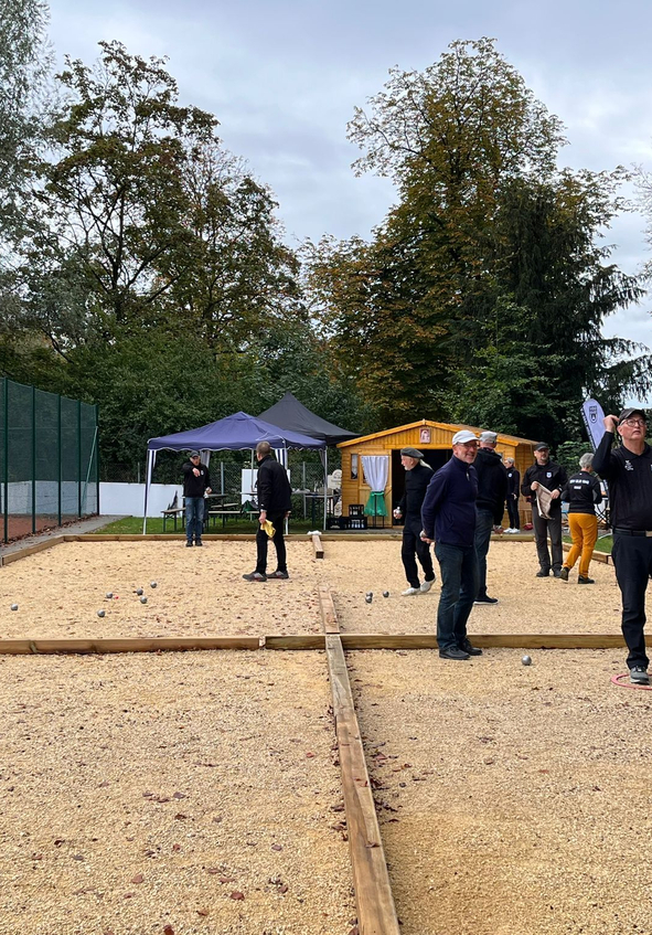 Mehrere Spieler werfen Metallkugeln auf Boule-Bahn mit Zelt