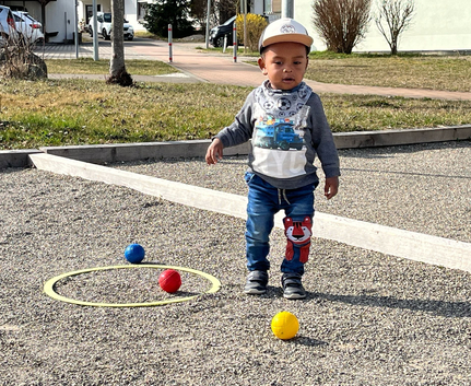 Kleines Kind auf Schotterplatz neben gelben roten und blauen Boulekugeln beim Freundschaftsturnier