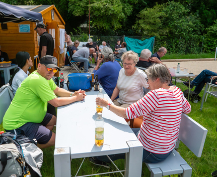 Personen sitzen an Außentisch mit Getränken vor Holzhütte
